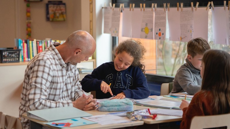 Onderwijsambassadeur Jan Joost in de klas zittend bij kinderen Onderwijsambassadeur in de klas. Jan Joost zittend bij kinderen.